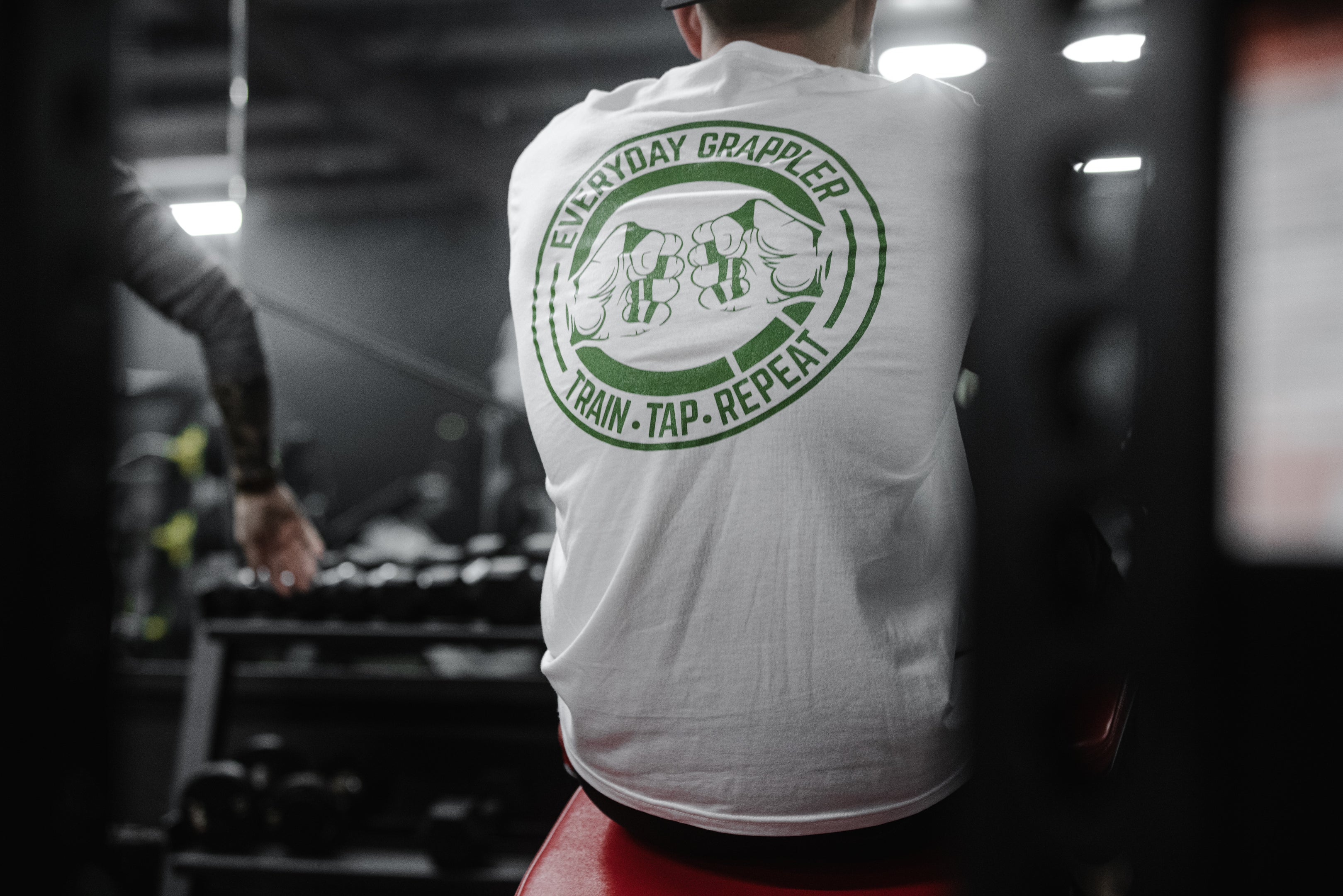 Athlete in the gym wearing the white Everyday Grappler jiu jitsu tee with the green fist-bump back logo