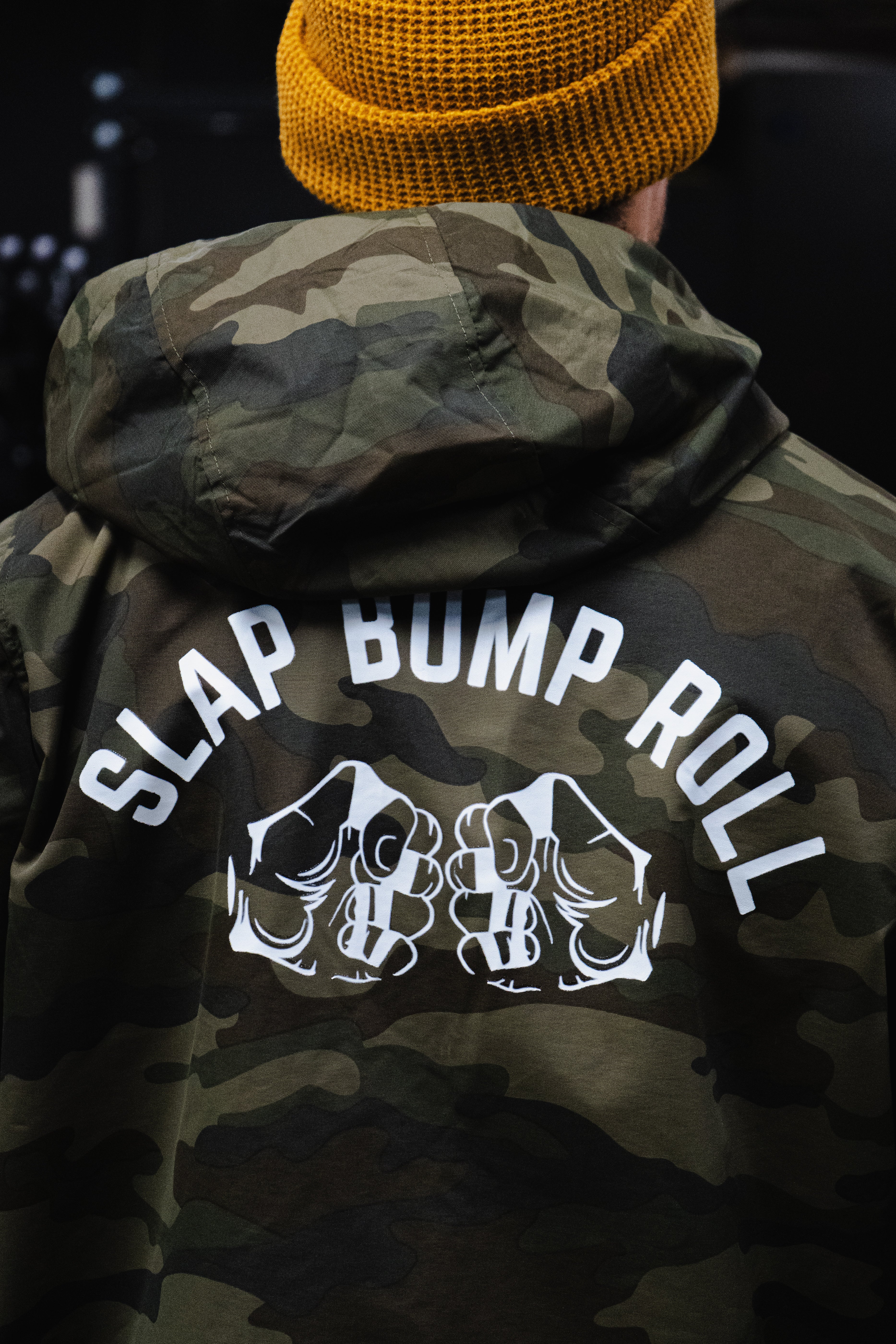 Detail shot of Slap Bump Roll fist bump graphic on back of SBR Camo Water-Resistant Windbreaker