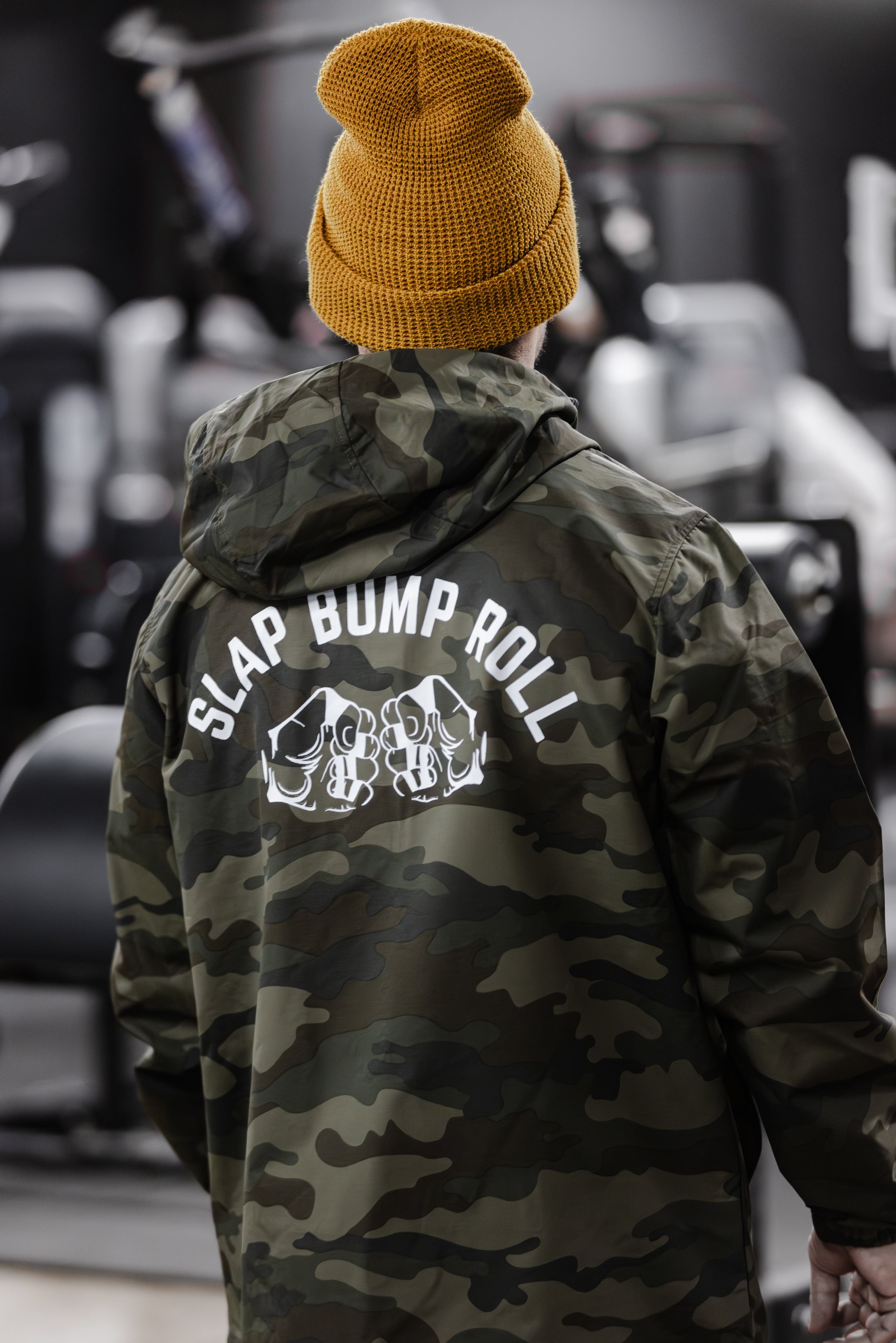 Athlete wearing SBR Camo Windbreaker in gym, back view showing Slap Bump Roll fist bump graphic in white