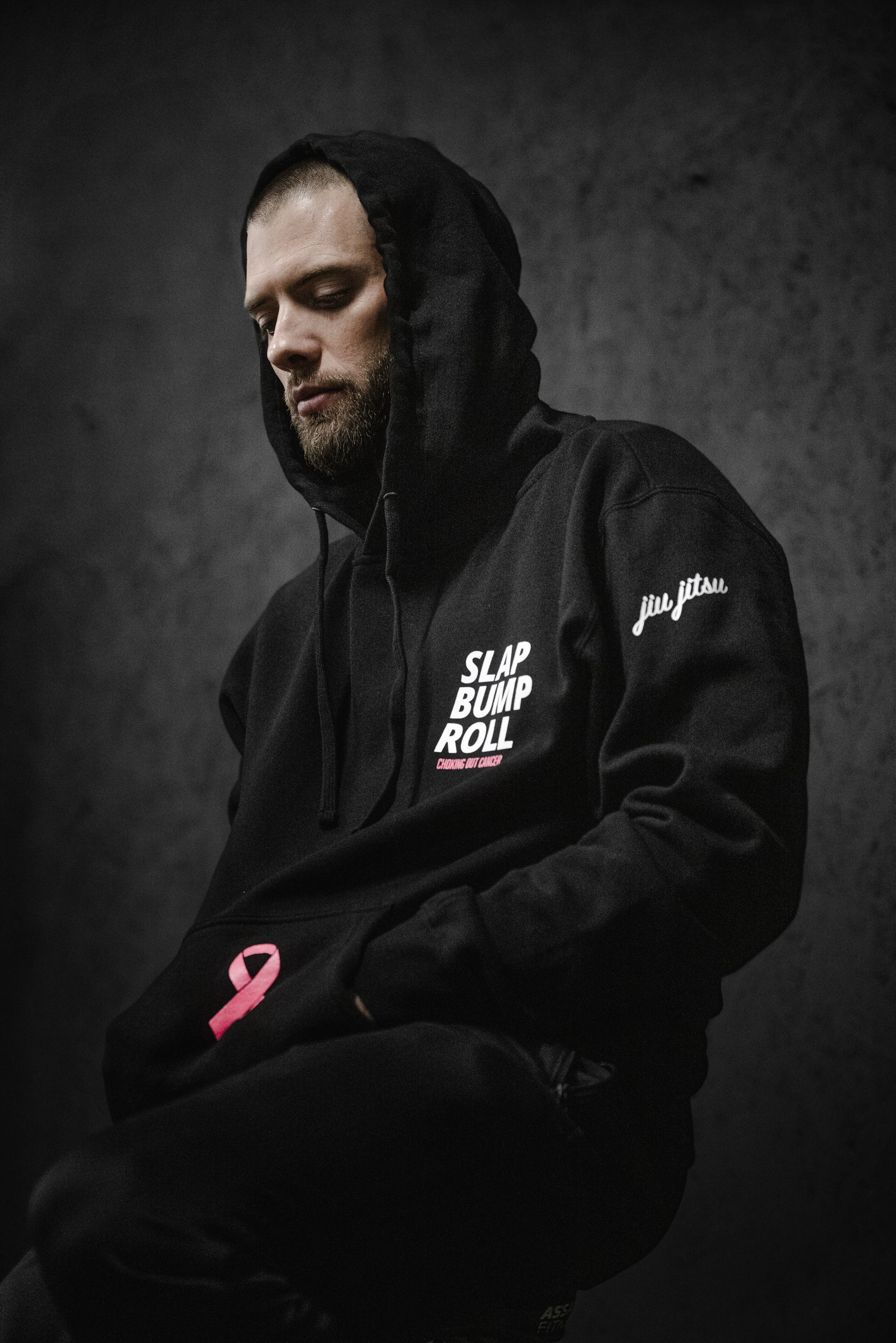 Man wearing SBR Choking Out Cancer Hoodie with hood up, black BJJ breast cancer awareness hoodie