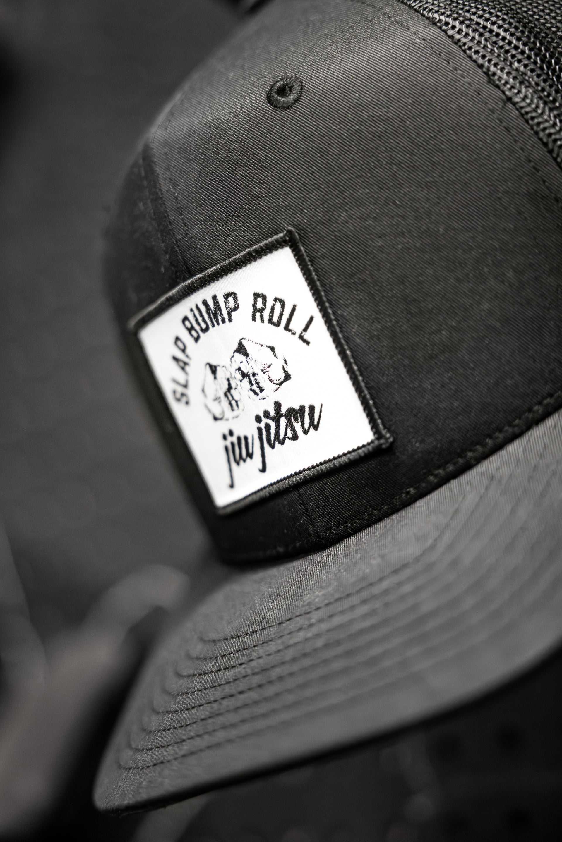 Front patch detail on SBR Jiu Jitsu Trucker Hat with Slap Bump Roll fist bump logo and jiu jitsu script