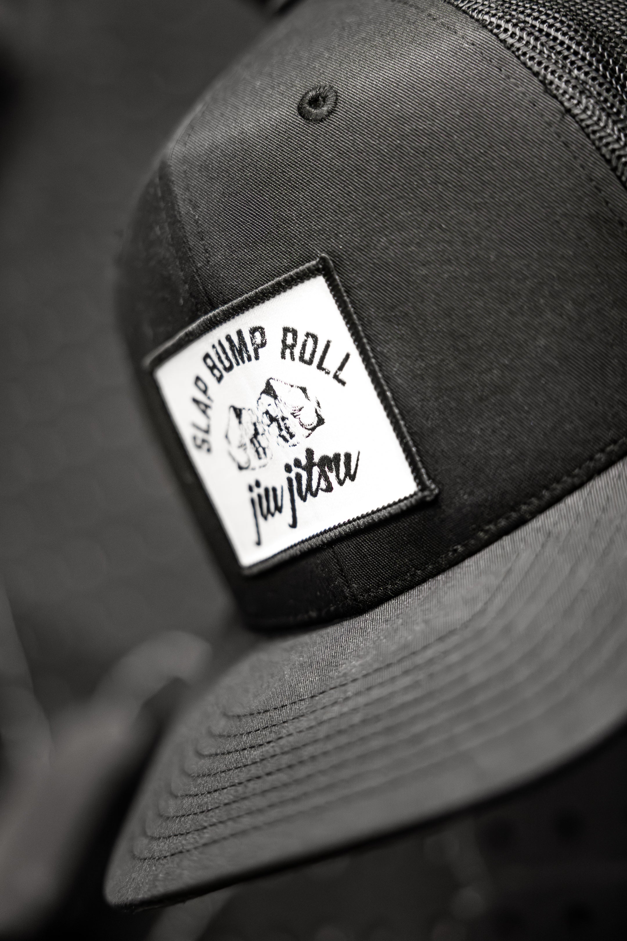 Front patch detail on SBR Jiu Jitsu Trucker Hat with Slap Bump Roll fist bump logo and jiu jitsu script