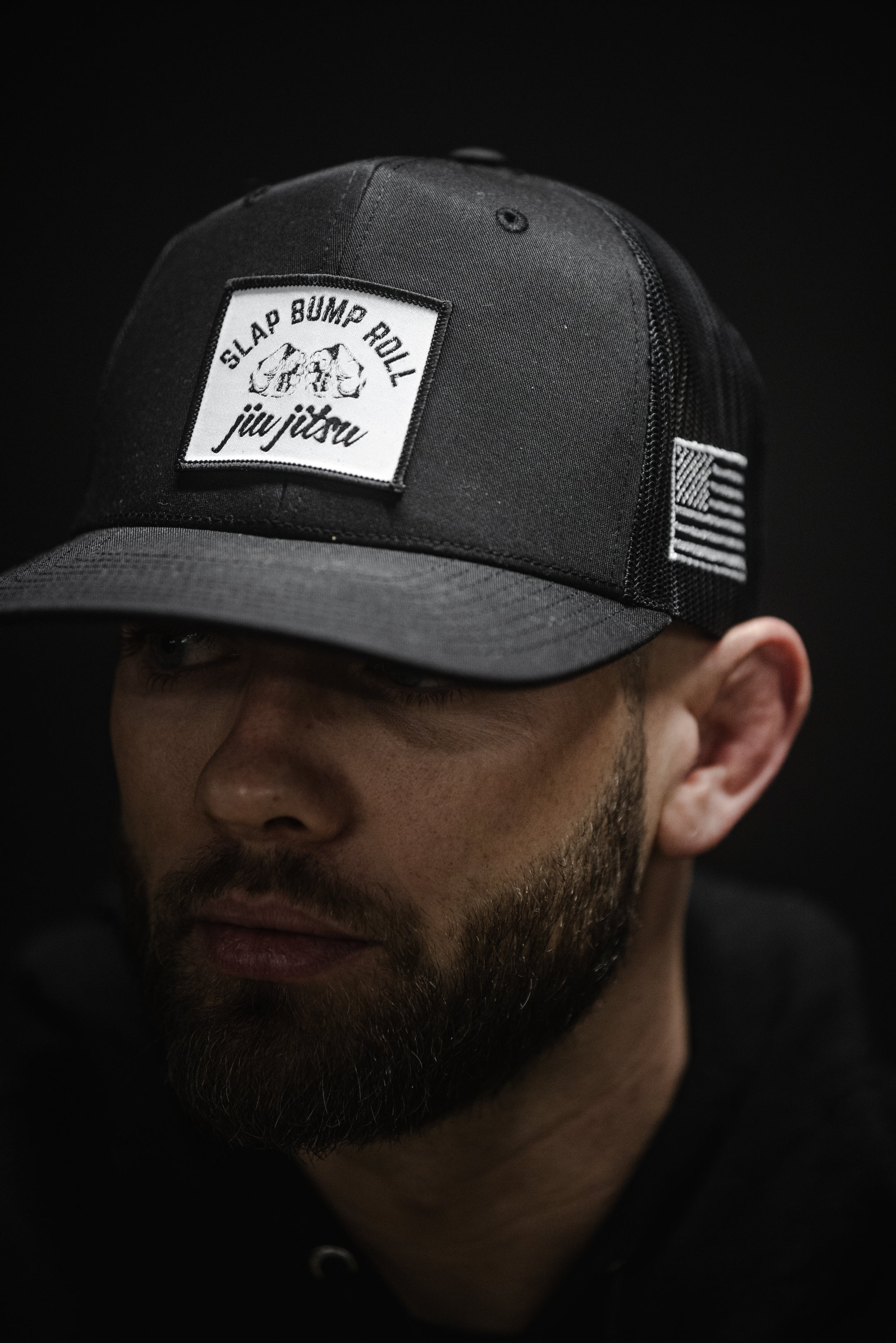Man wearing SBR Jiu Jitsu Trucker Hat in black, front view showing Slap Bump Roll fist bump patch