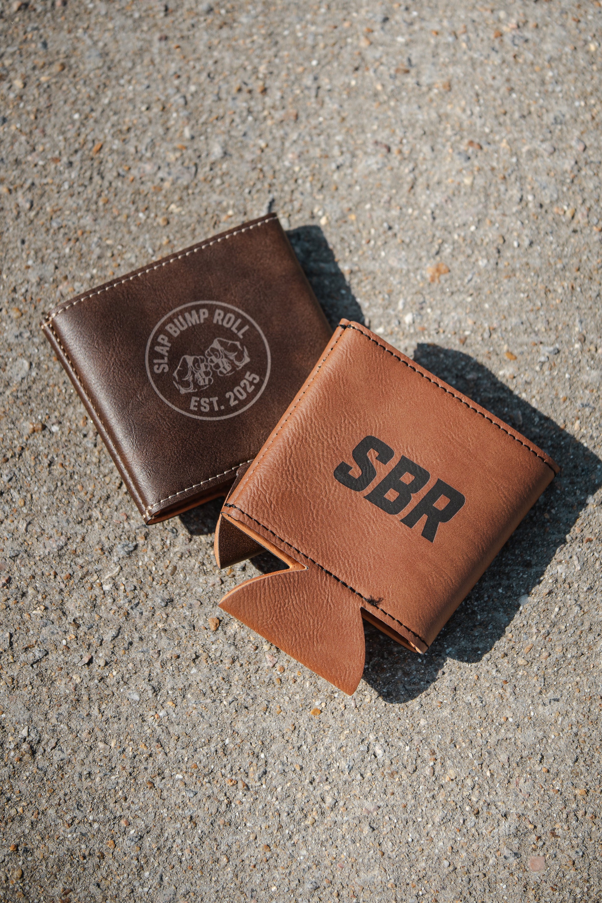 SBR Leatherette Koozies, dark brown with Slap Bump Roll circle logo and tan with bold SBR text, on concrete background