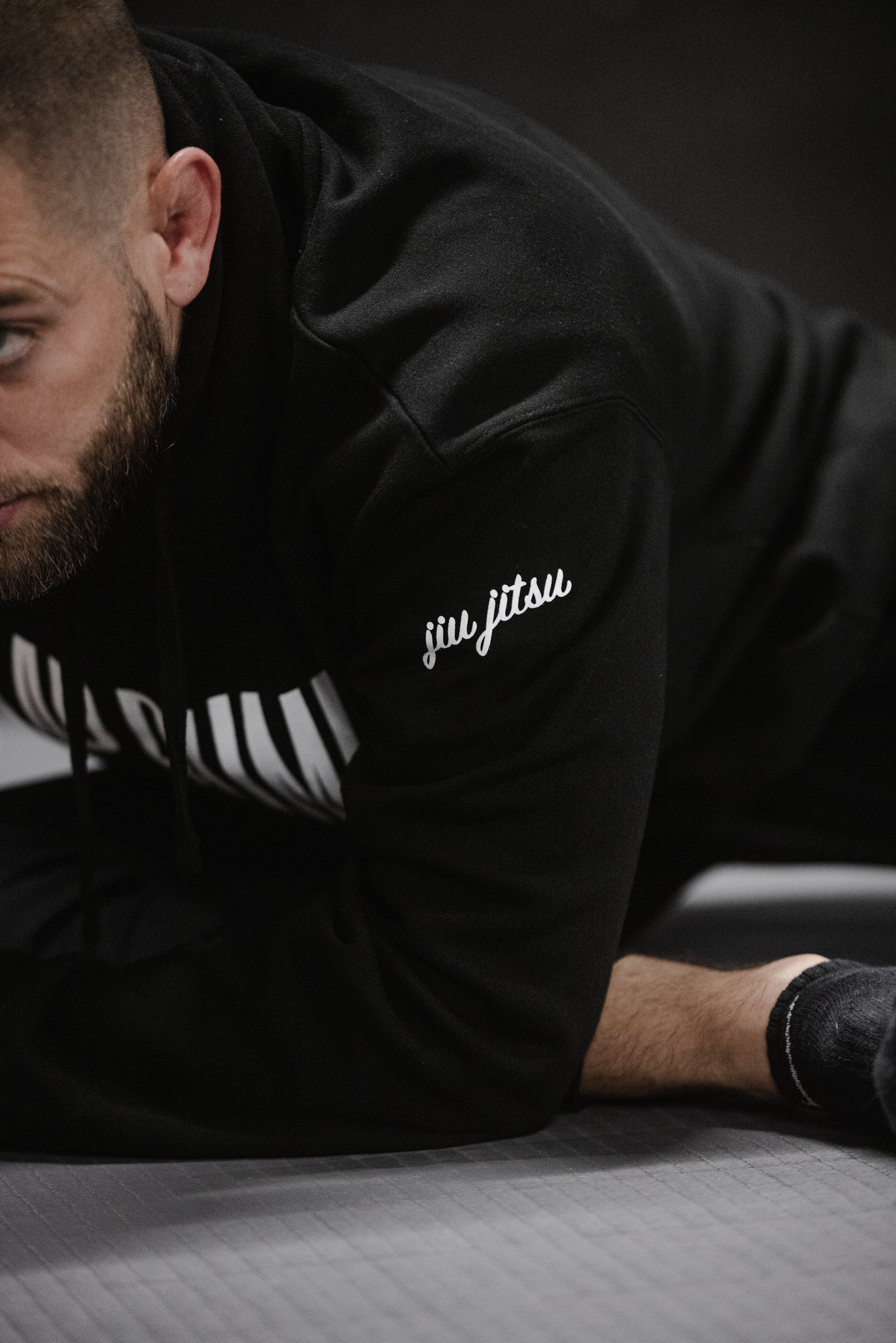 BJJ athlete on the mat showing the jiu jitsu script embroidery on the sleeve of the black Slap Bump Roll hoodie