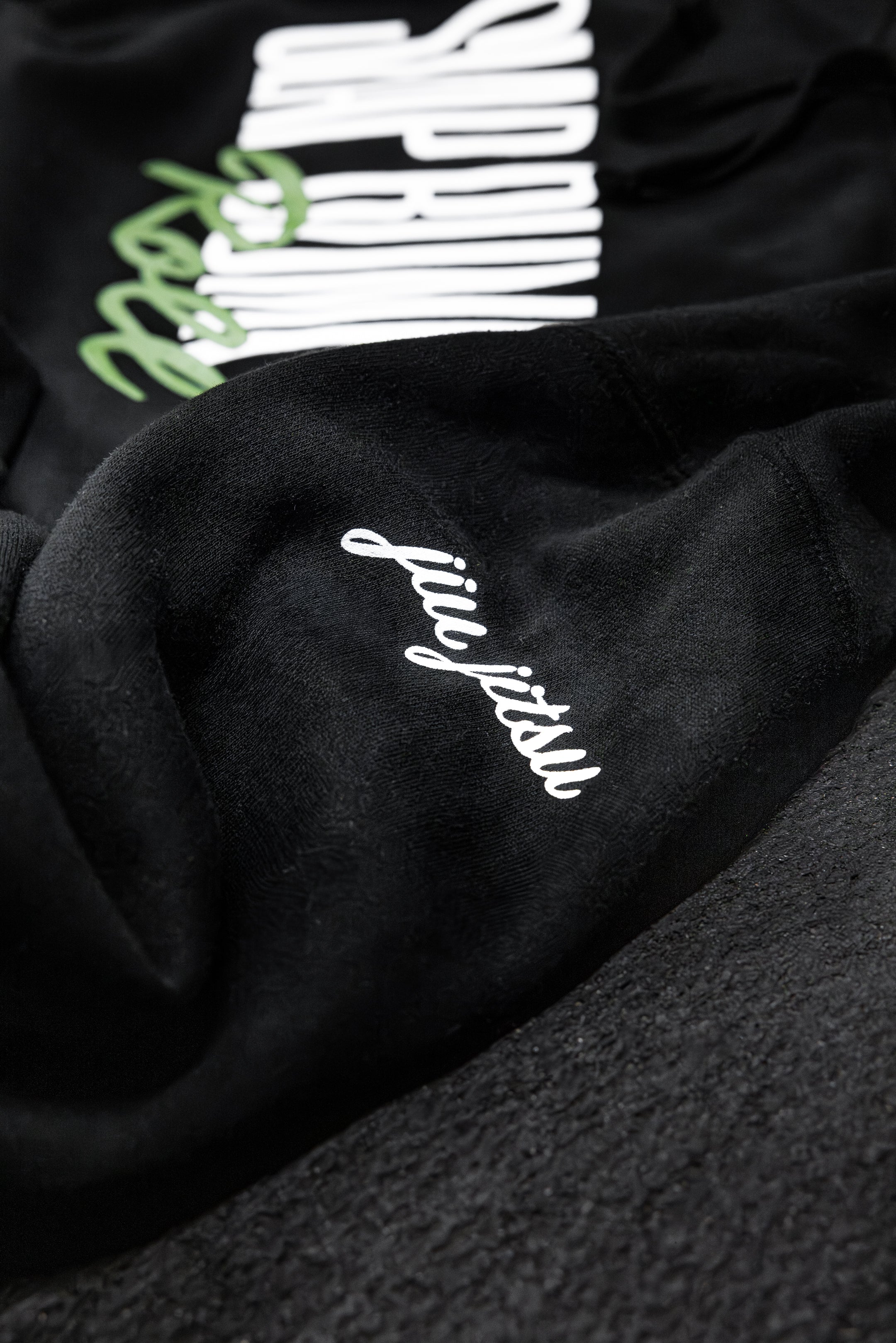 Close-up of jiu jitsu script embroidery on the sleeve of the black Slap Bump Roll BJJ hoodie with soft fleece interior