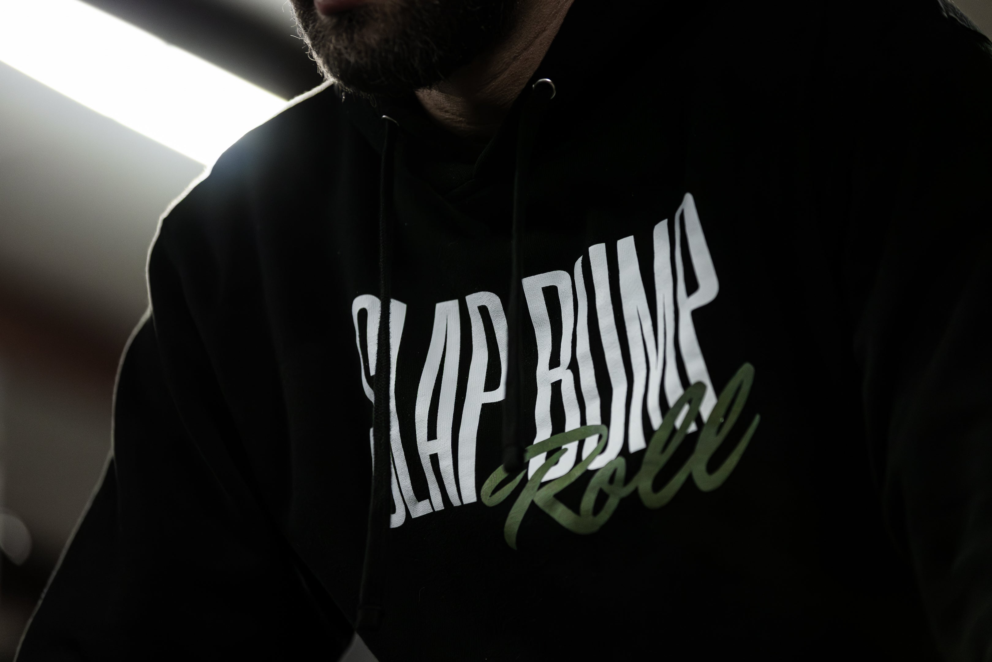 Low-light close-up of the SLAP BUMP ROLL wordmark on the black midweight BJJ hoodie by Slap Bump Roll