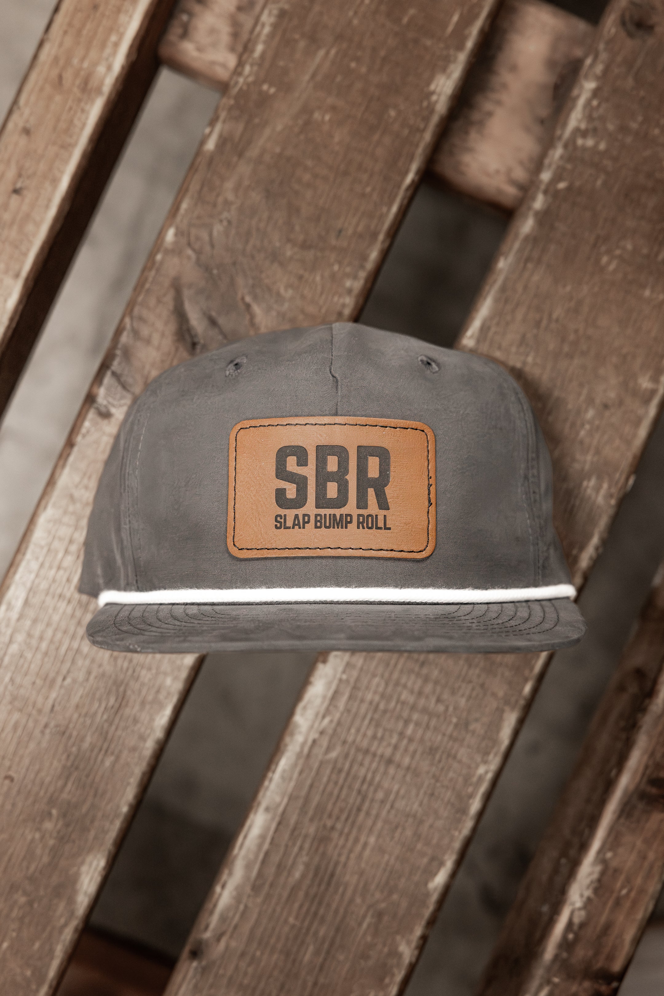 Charcoal Slap Bump Roll five-panel rope snapback with leather SBR patch resting on weathered wood