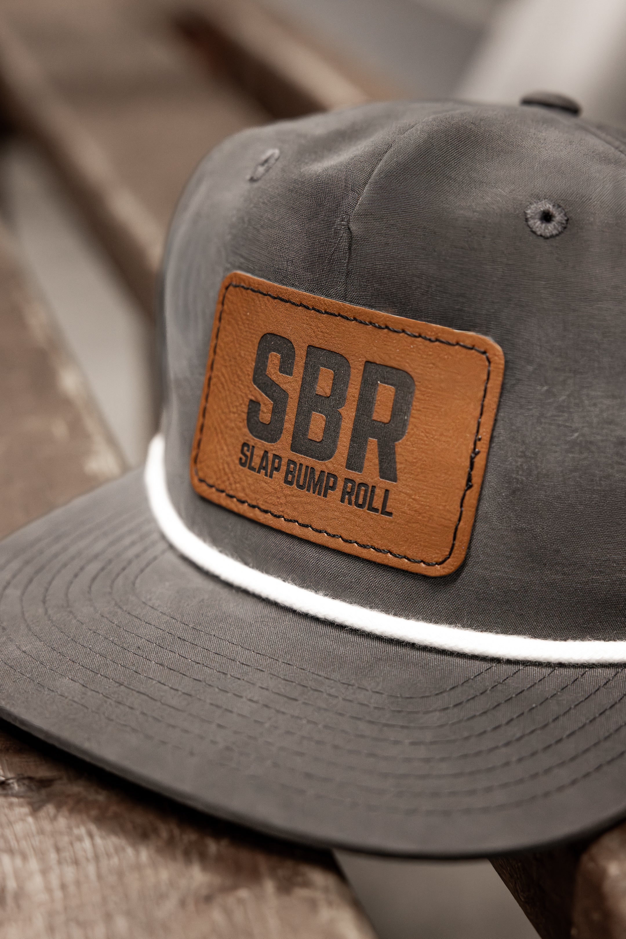 Close-up of the tan leather SBR Slap Bump Roll patch and white rope braid on the charcoal snapback cap