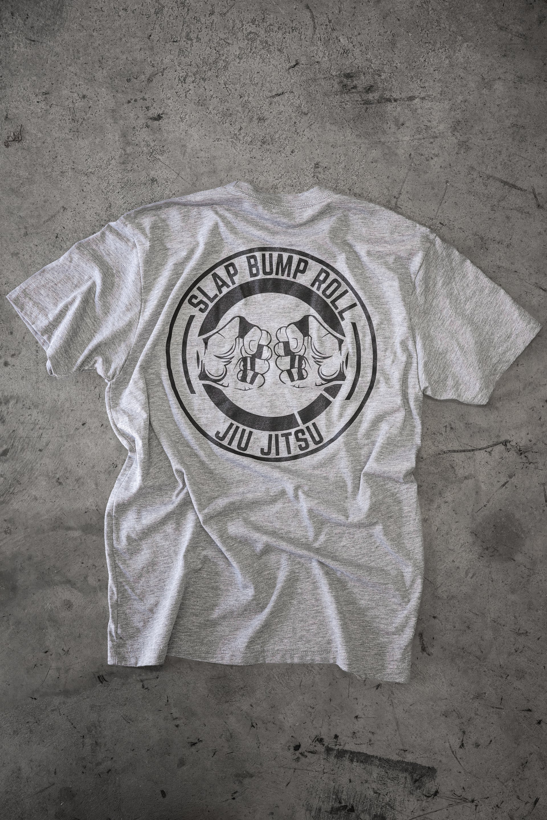 Back of the heather grey Slap Bump Roll BJJ tee with the circular SLAP BUMP ROLL JIU JITSU fist-bump logo