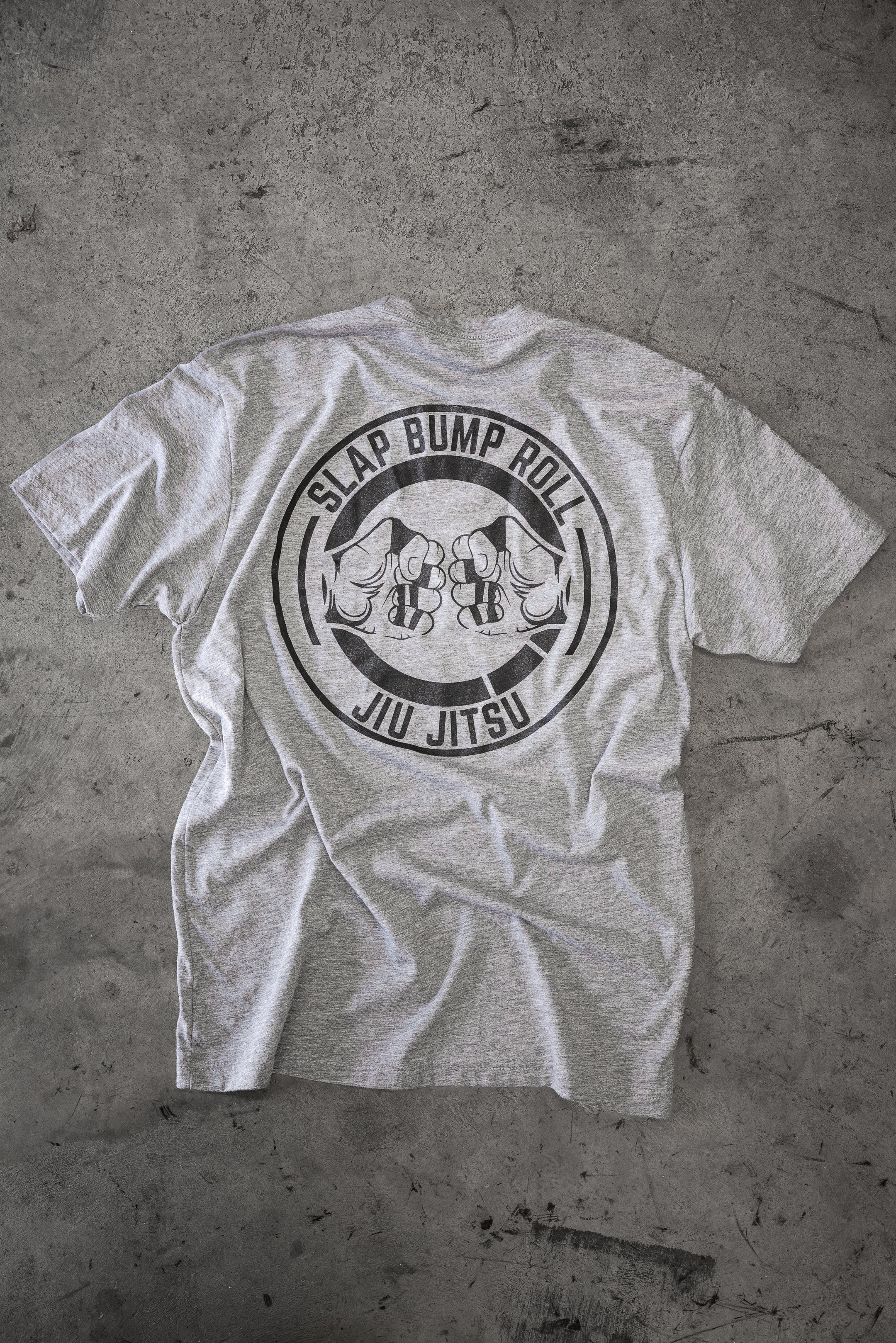 Back of the heather grey Slap Bump Roll BJJ tee with the circular SLAP BUMP ROLL JIU JITSU fist-bump logo