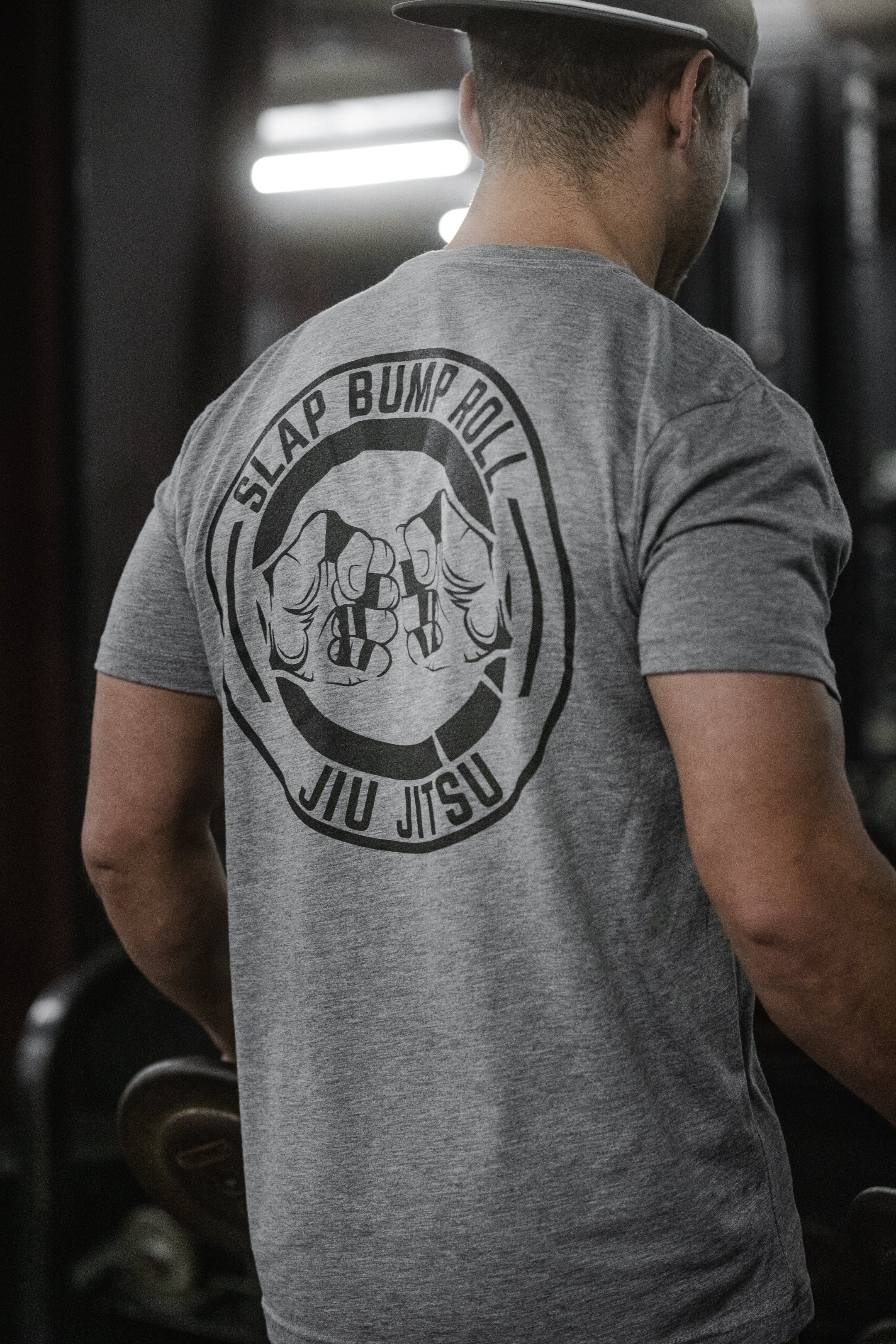 Lifter in the gym wearing the heather grey Slap Bump Roll BJJ tee with the fist-bump logo across the back
