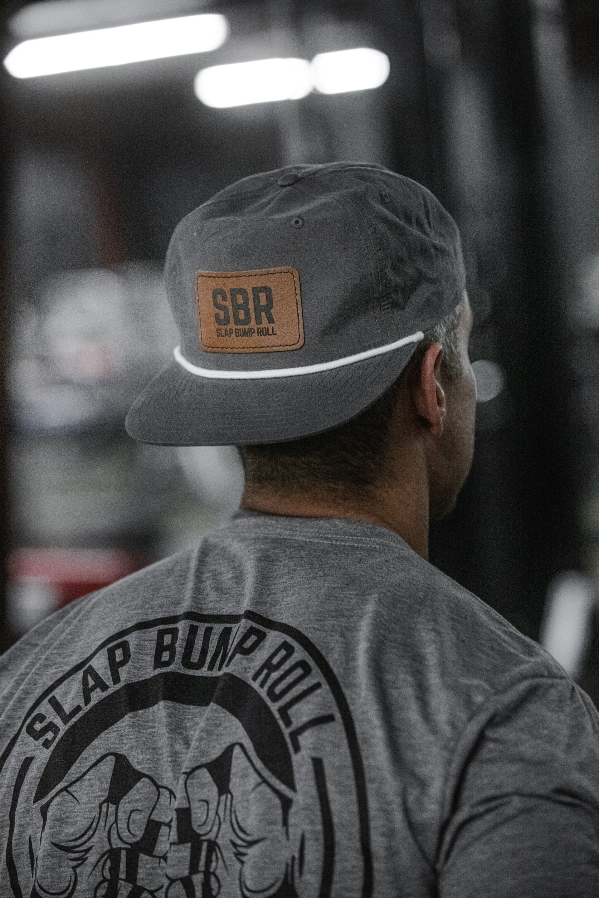Back view of the heather grey Slap Bump Roll jiu jitsu tee with the circular mat tap logo, worn in the gym