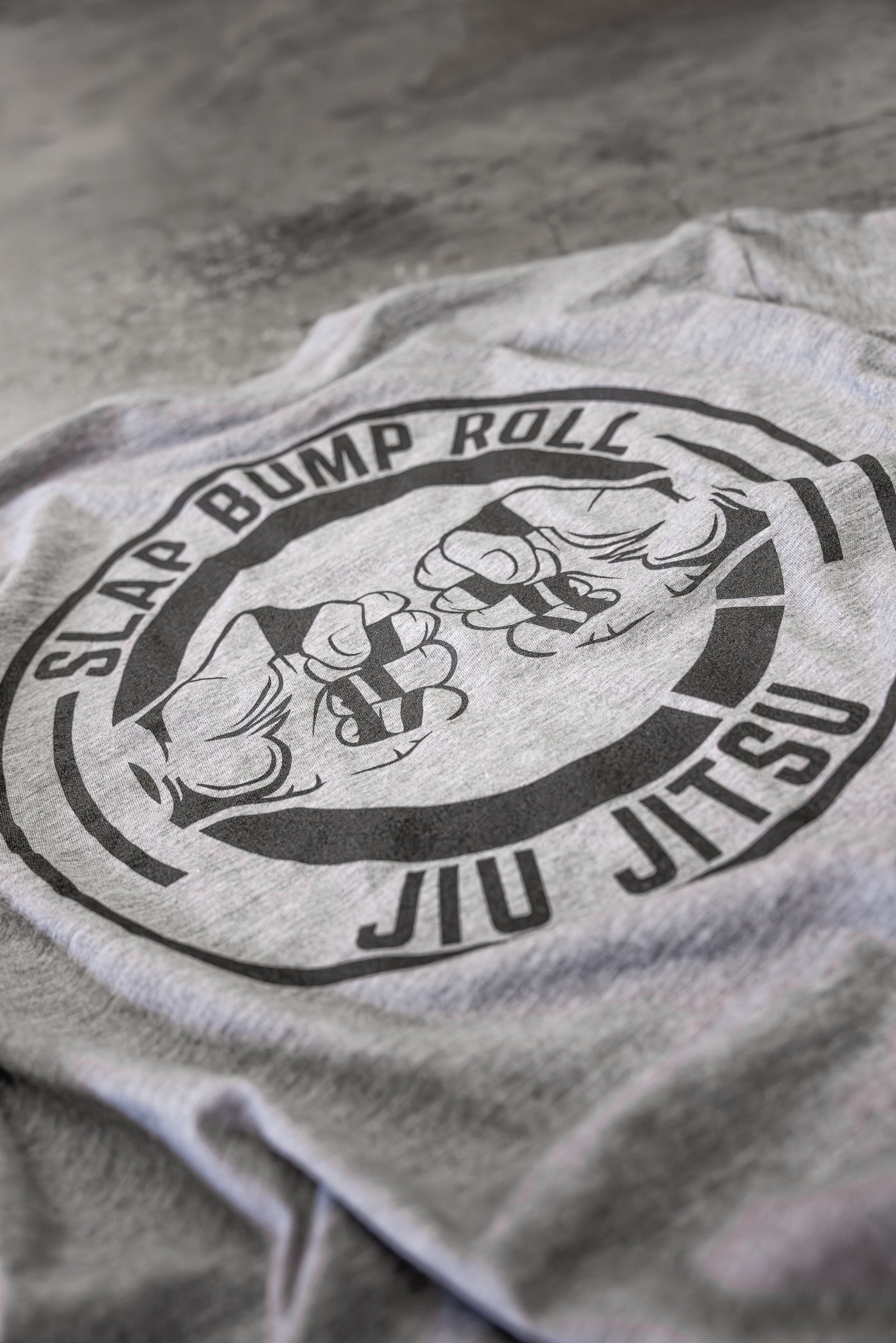 Close-up of the fist-bump mat tap logo and SLAP BUMP ROLL JIU JITSU text on the back of the tri-blend tee