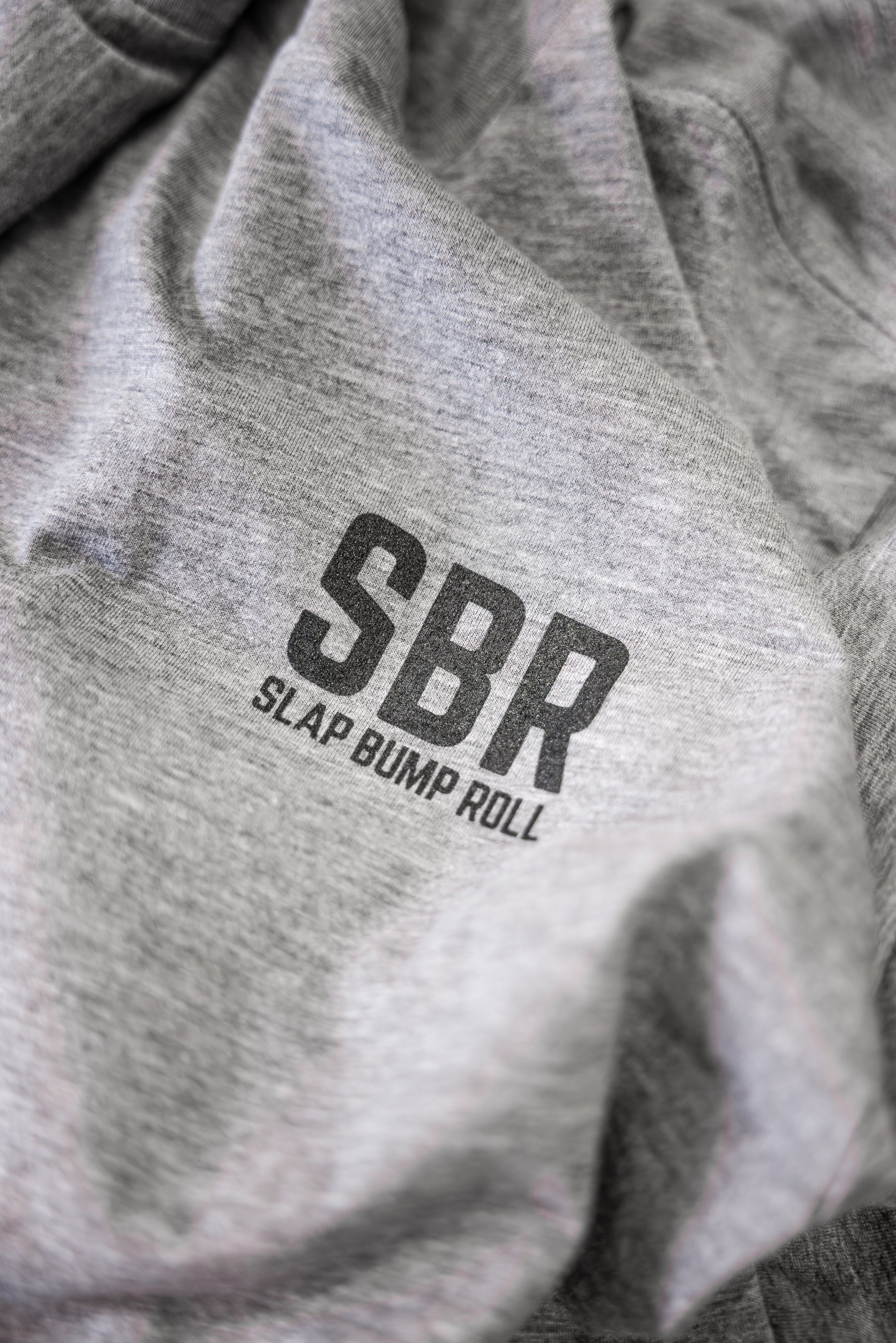 Close-up of the SBR Slap Bump Roll wordmark on the chest of the soft heather grey tri-blend jiu jitsu tee
